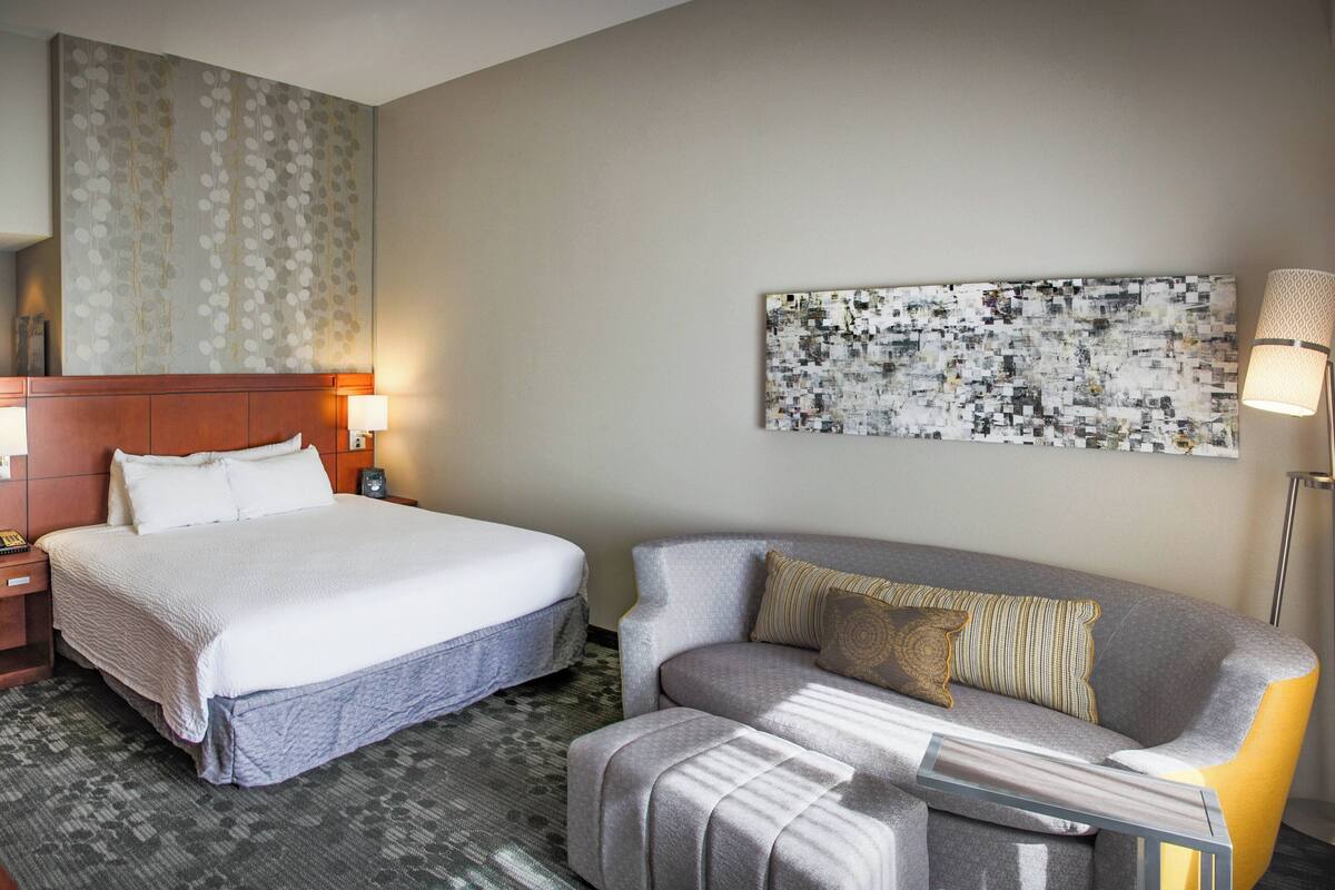 A hotel room with a bed, a sofa, a large abstract painting, and a lamp.