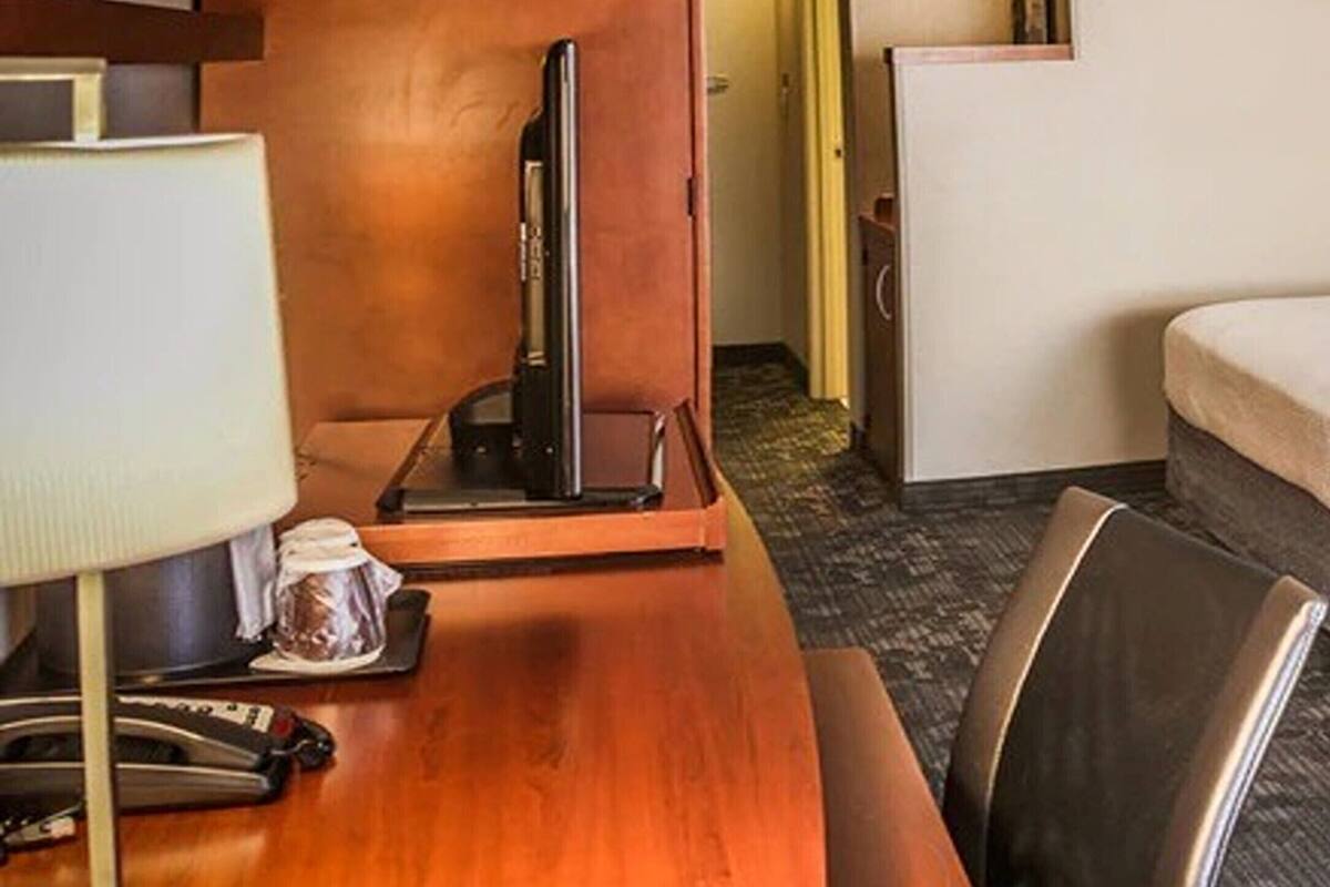 A hotel room with a wooden desk, a television, a lamp, and a bed.
