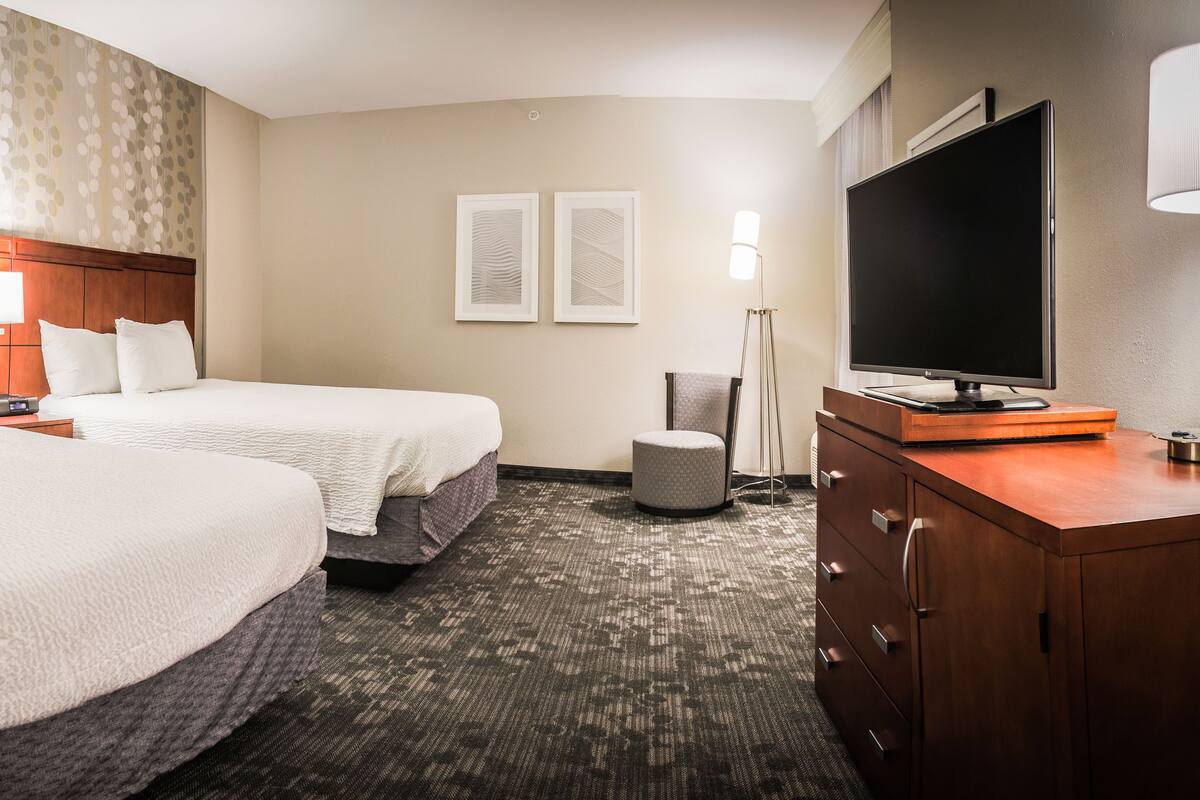 A hotel room with two beds, a flat-screen TV, a desk, and a lamp.