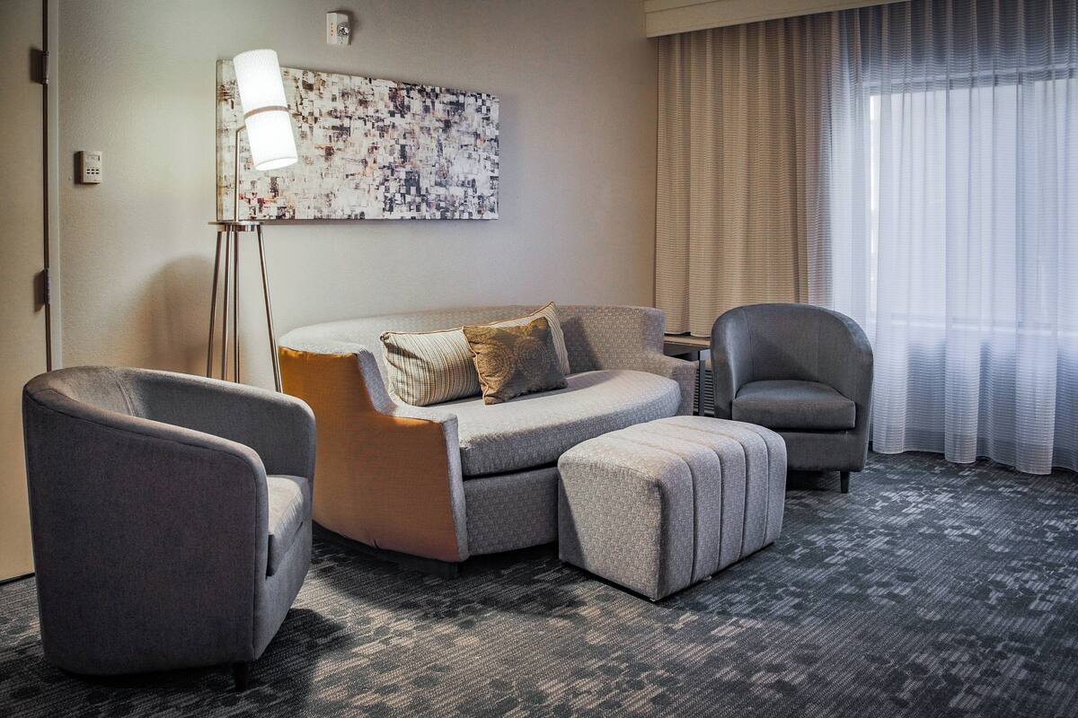 A modern hotel room with a grey sofa set, a floor lamp, and a large abstract painting on the wall.