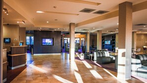 A spacious lobby with a reception desk, seating areas, and a television screen.