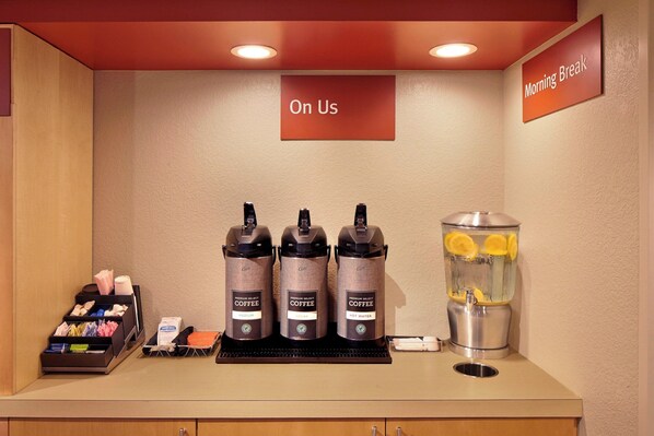 A coffee station with three coffee dispensers, a water dispenser, and a tray with various coffee pods and utensils.