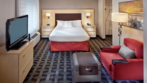 A hotel room with a bed, a TV, a red sofa, a small table, and a lamp.