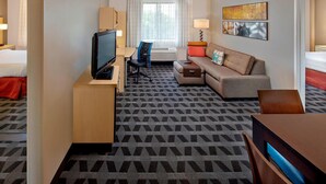 A hotel room with a bed, a desk with a TV, a sofa, a chair, and a patterned carpet.