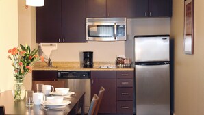 A compact kitchen with dark cabinets, a stainless steel refrigerator, a microwave, and a coffee maker.