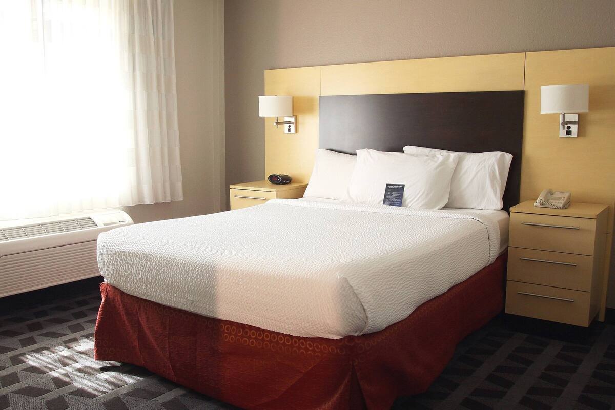 Una habitación de hotel con una cama grande, dos mesitas de noche, un calefactor y una ventana con cortinas.