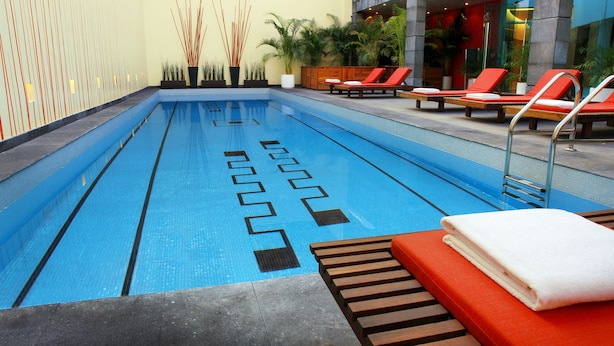 Una piscina interior con carriles delimitados, sillas reclinables rojas y suelo de baldosas.