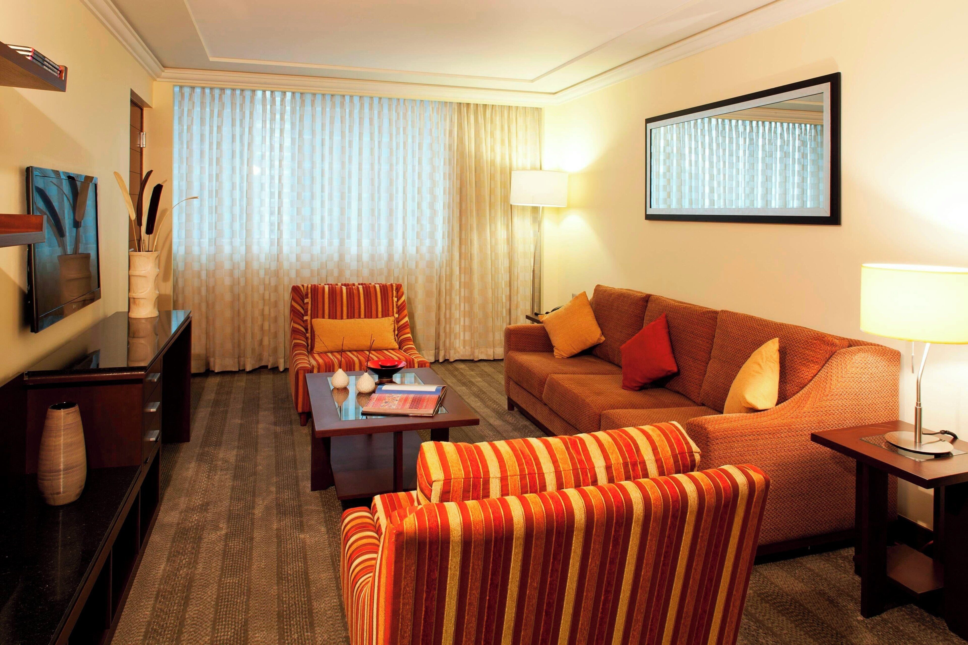 Una camera d'hotel con un divano a righe, una poltrona coordinata, un tavolino e un'ampia finestra con tende.