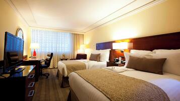 A hotel room with two beds, a desk, a chair, and a TV.