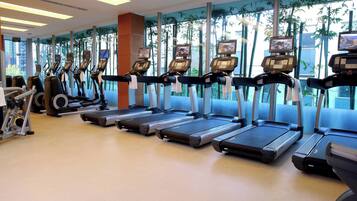 Un gimnasio con varias cintas de correr, bicicletas estáticas y un ventanal con vistas a árboles.