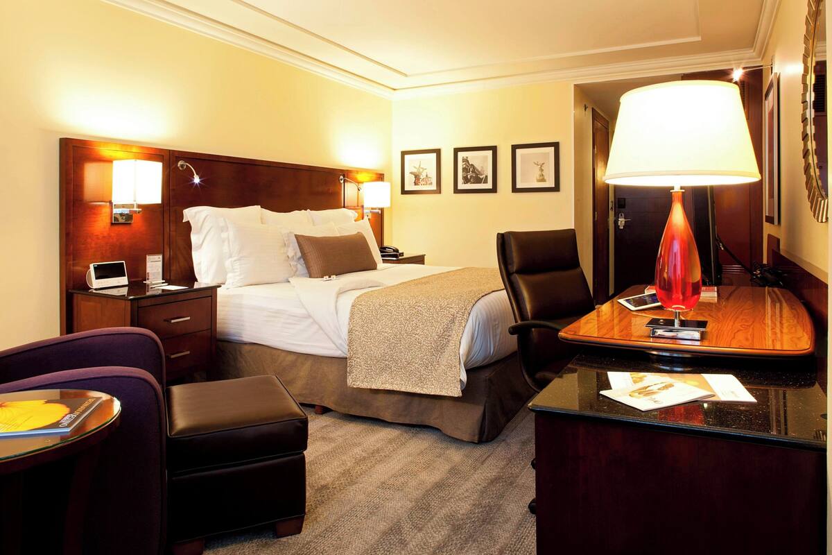 Habitació d'hotel amb llit, taula de nit, làmpada, cadira i escriptori.