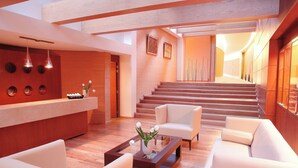 Un vestíbulo moderno con mostrador de recepción, zona de estar y una escalera que conduce a los pisos superiores.