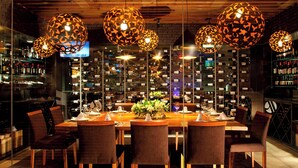 Un restaurante con una larga mesa de madera dispuesta para comer, rodeada de sillas e iluminada por luces esféricas con diseños.