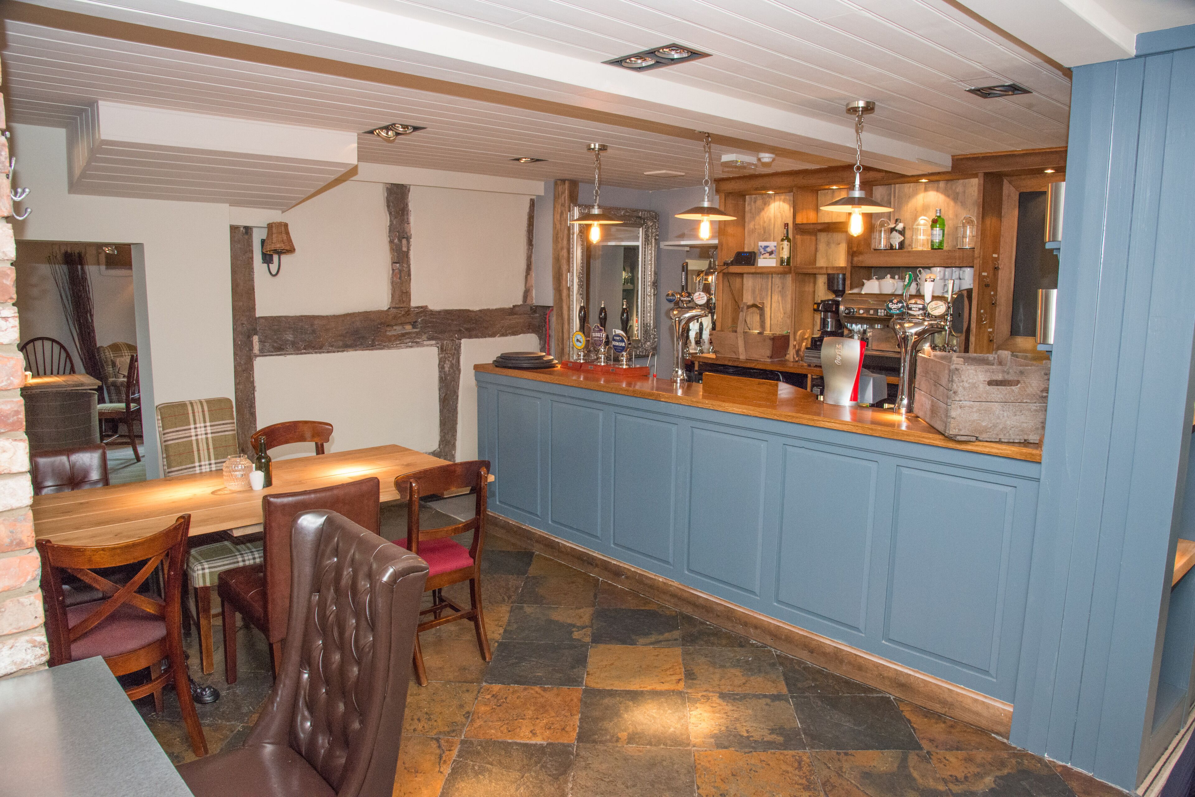 Un comedor con mesa y sillas de madera, una zona de bar con un armario azul y un suelo de baldosas.