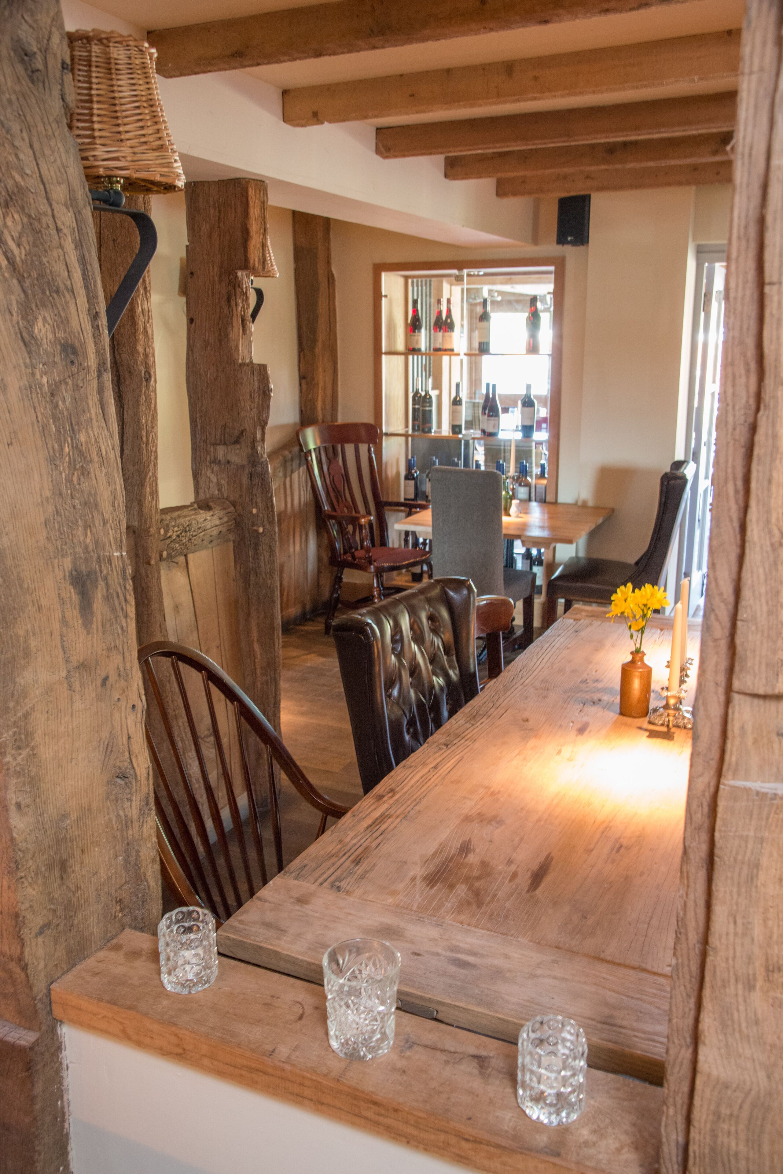 Un comedor rústico con una mesa de madera, sillas de cuero y una vista de botellas de vino al fondo.