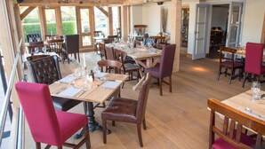 A restaurant with wooden beams, large windows, and multiple dining tables set for guests. - The Swan Inn (Worcester)