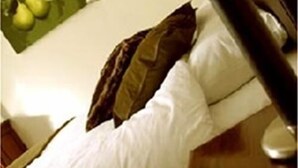 A bed with white sheets and a brown pillow, a green wall with a fruit picture, and a nightstand with a lamp. - The Swan Inn (Worcester)
