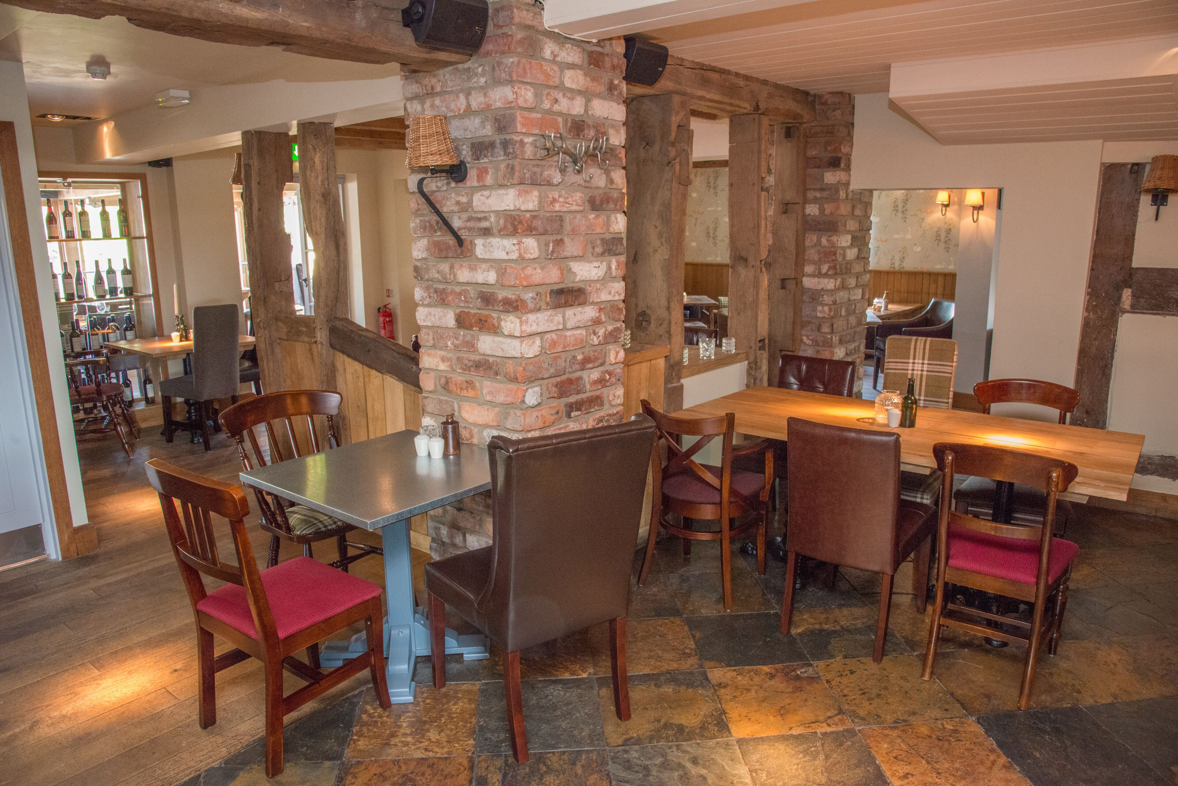 A restaurant with a brick column, wooden tables and chairs, and a bar area in the background.