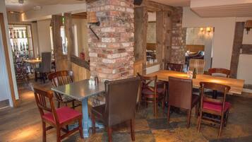 A restaurant with a brick column, wooden tables and chairs, and a bar area in the background.