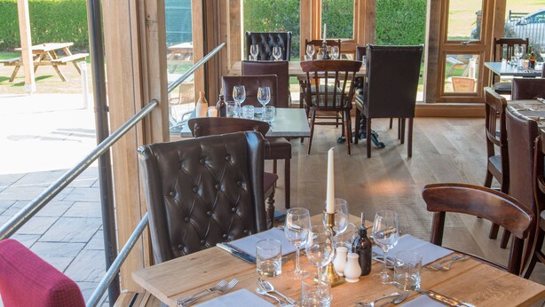 A restaurant with wooden beams, large windows, and a mix of red and brown upholstered chairs. - The Swan Inn (Worcester)