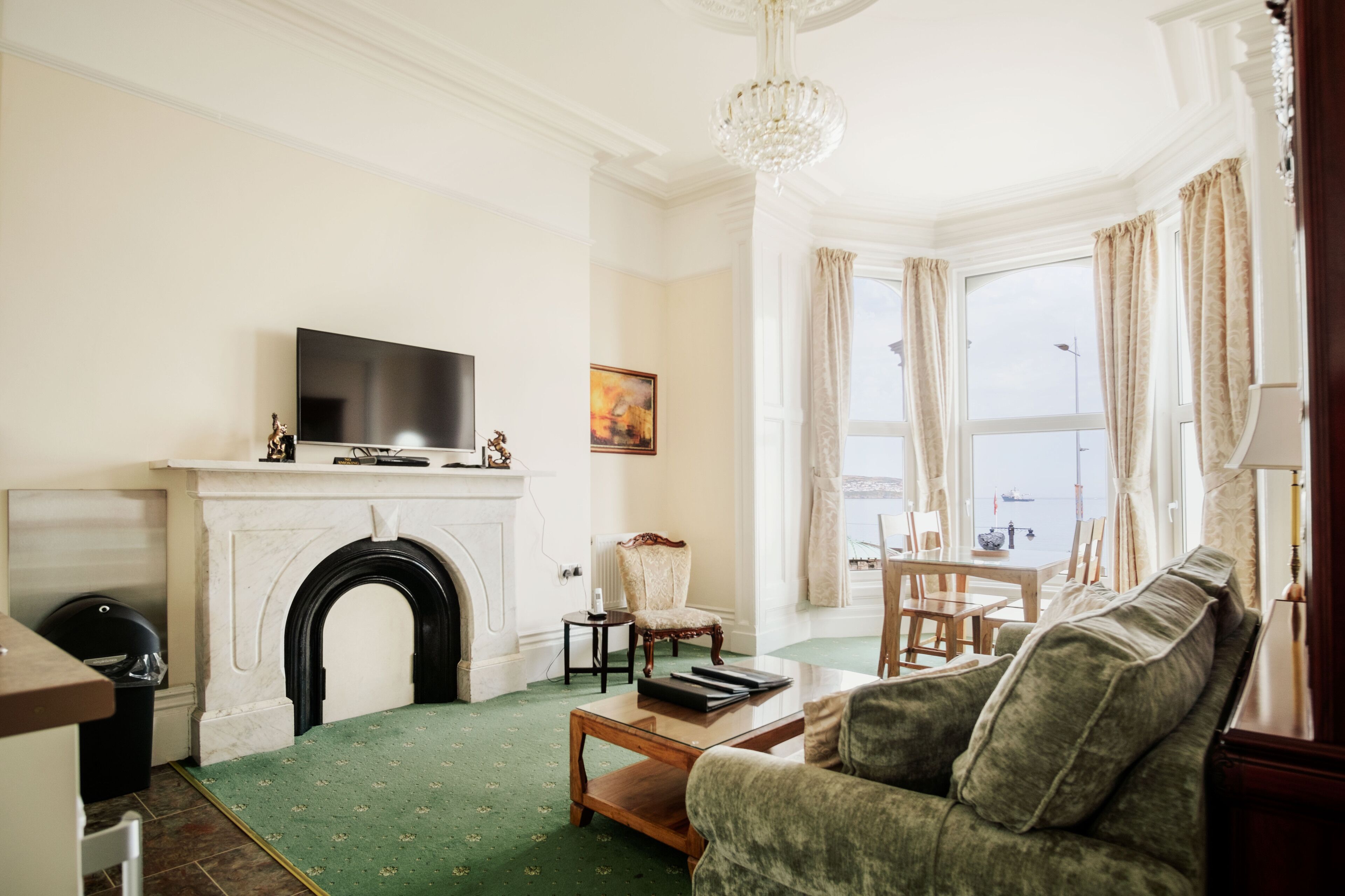A living room with a fireplace, a television, a sofa, and a view of the sea.