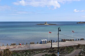 Vista costera con un faro, playa e instalaciones portuarias.