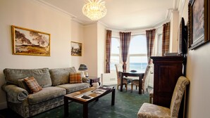 A living room with a sofa, armchair, coffee table, and a view of the sea through large windows.