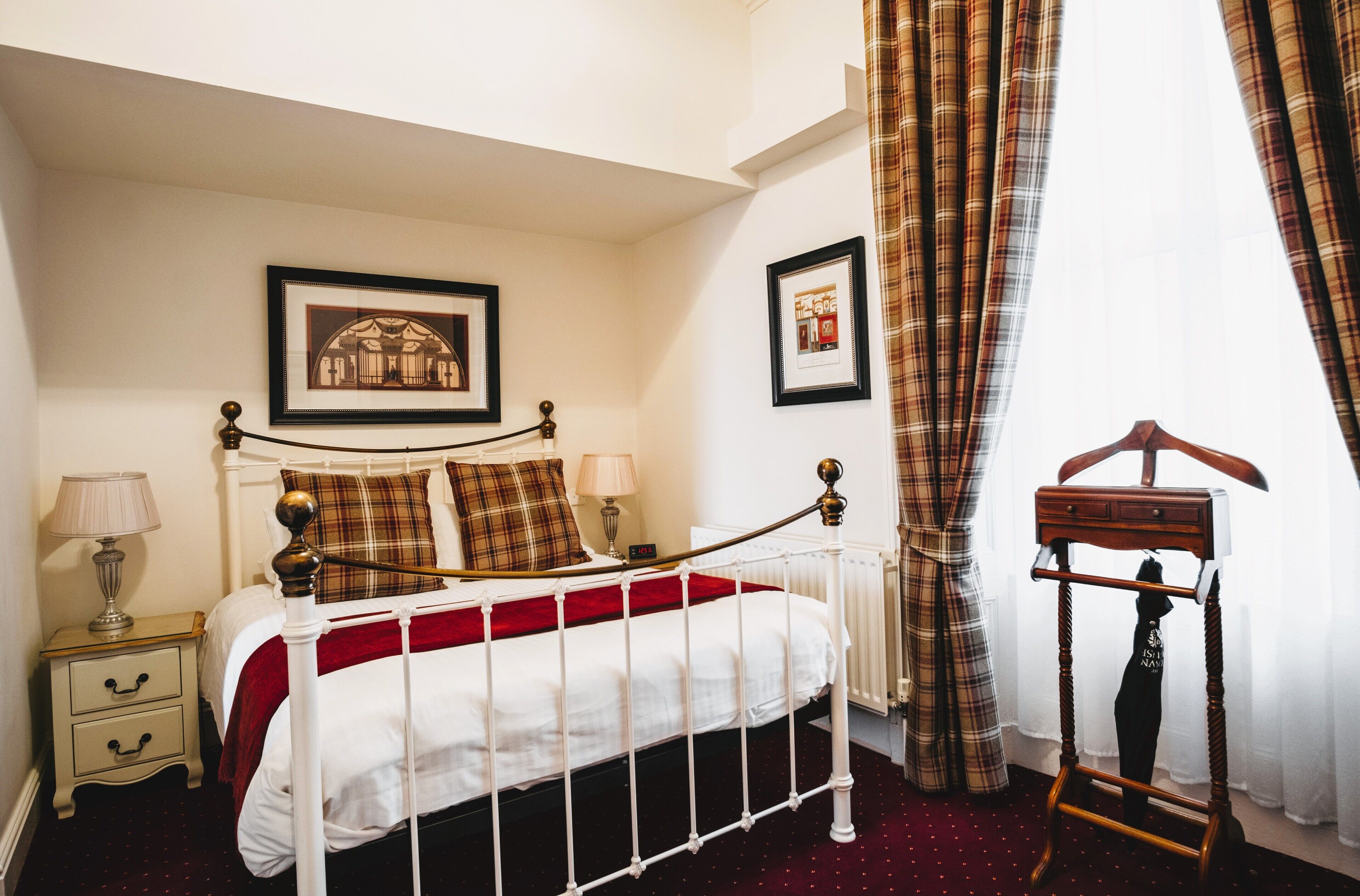 A neatly arranged bedroom with a bed, bedside tables, a radiator, and a hanging coat rack.
