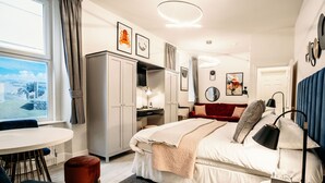 A modern bedroom with a bed, bedside table, lamp, and a view of a cityscape through a window.