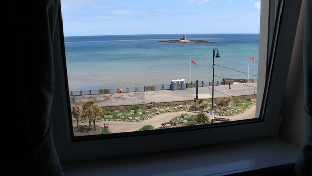 A view from a window overlooking a beach with a small island, a sandy area with a fence, and a few people.