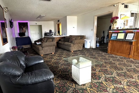 A living room with a black leather sofa, two brown armchairs, a glass coffee table, and a patterned carpet.. Super Value Inn Richland Near Americus US 280