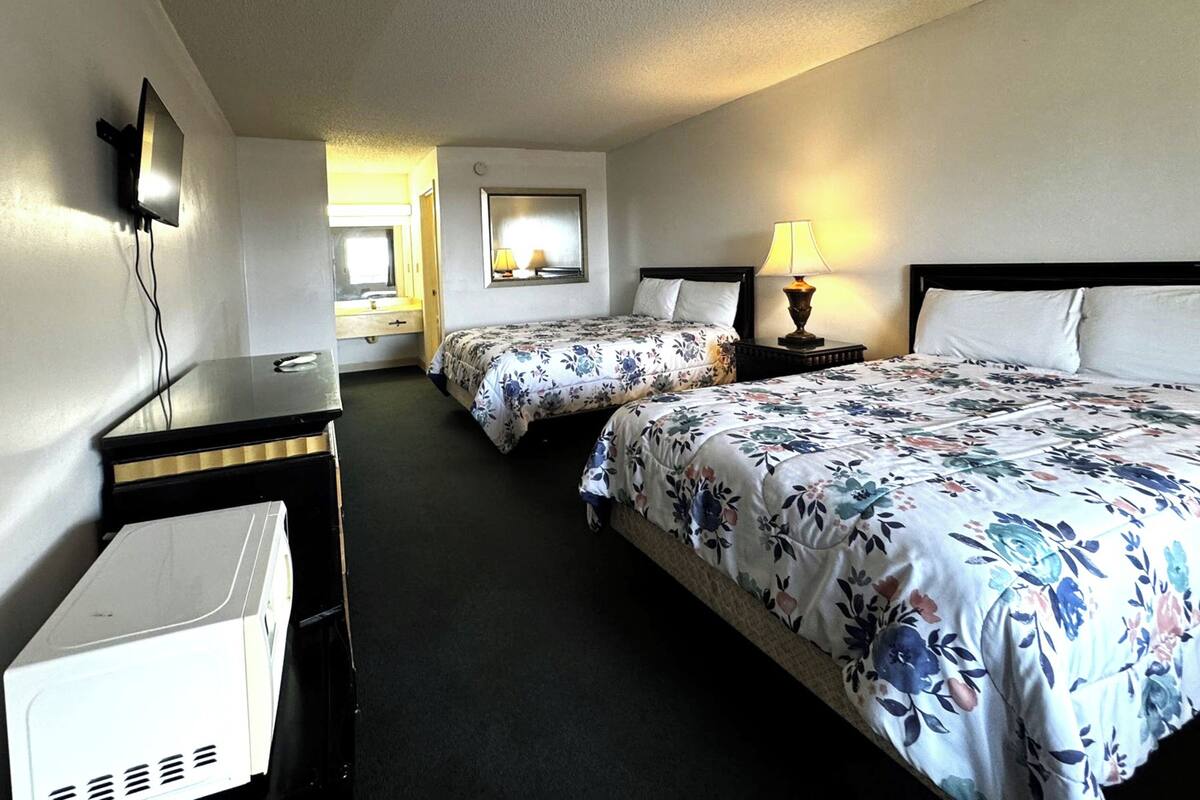 A hotel room with two beds, a desk, a TV, and a window.