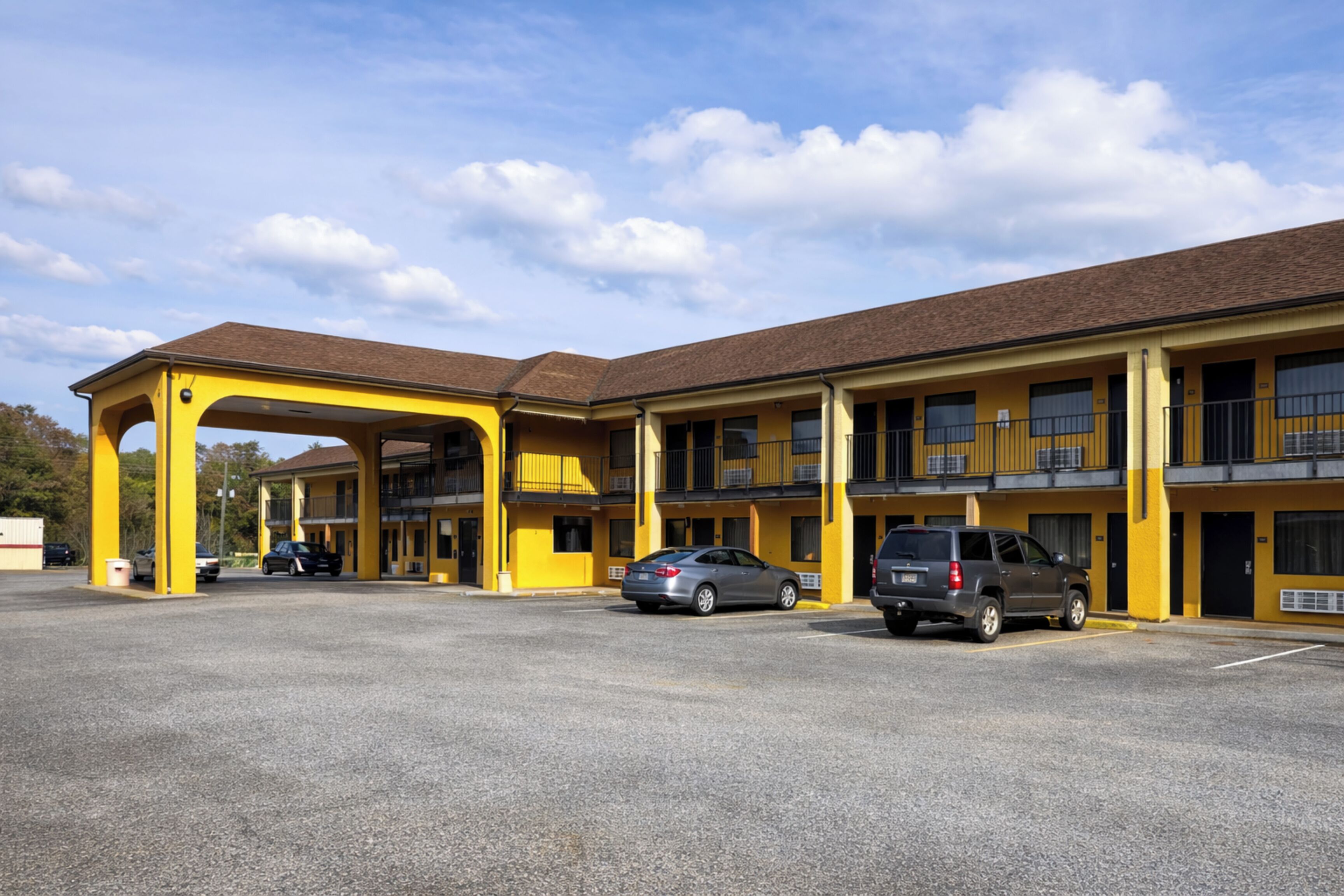 Un motel con fachada amarilla, varios balcones y un estacionamiento con varios coches.