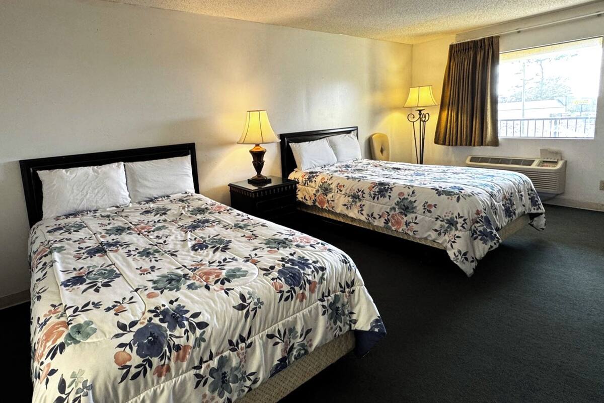 A hotel room with two beds, each with floral bedding, bedside lamps, and a window with curtains.