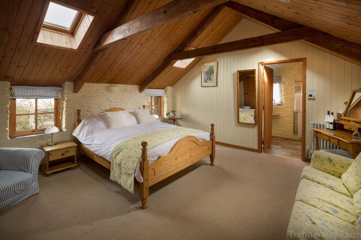 A cozy bedroom with a wooden bed, a small bedside table, a chair, and a large window.