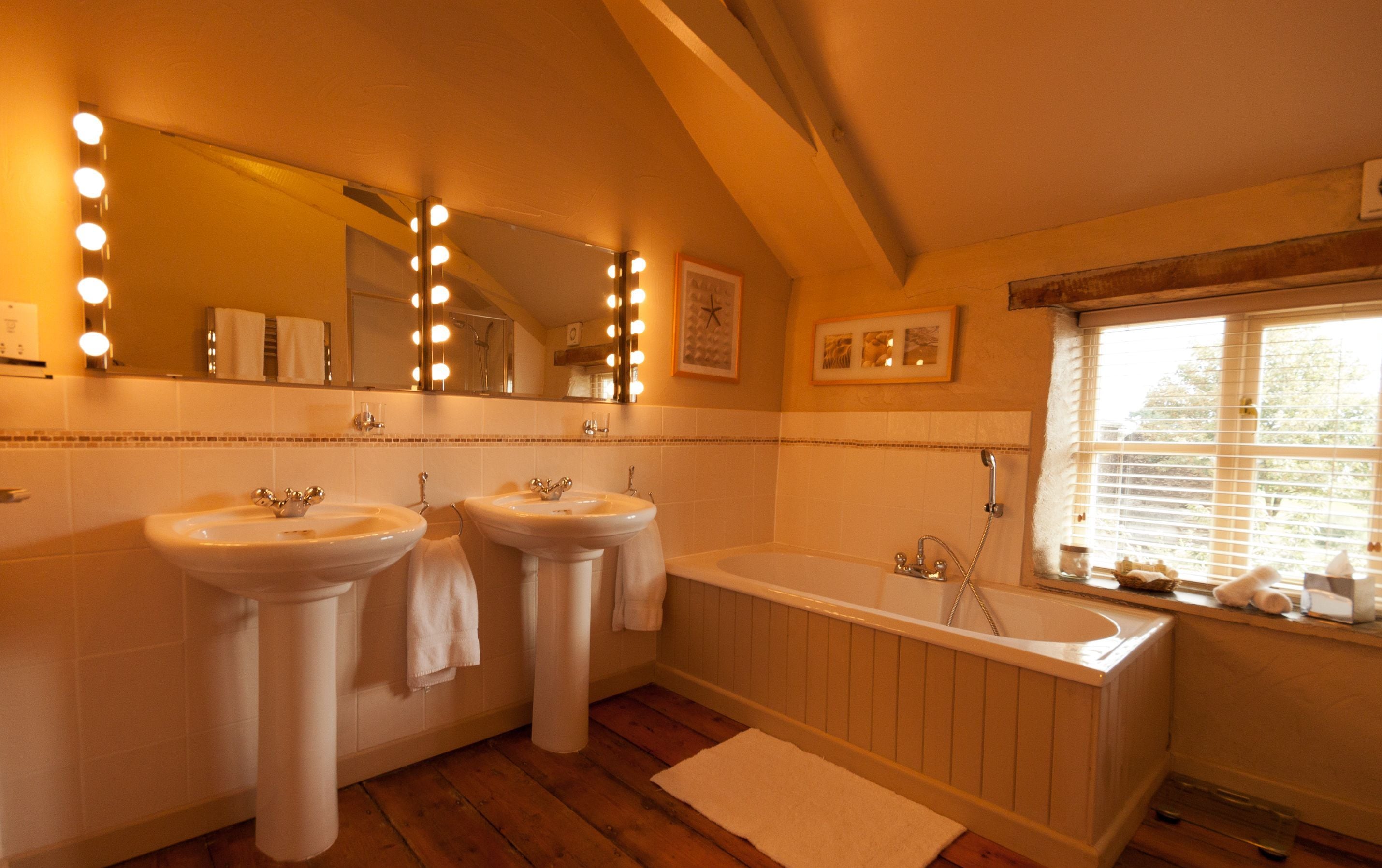 A bathroom with two sinks, a bathtub, and a large mirror with lights.
