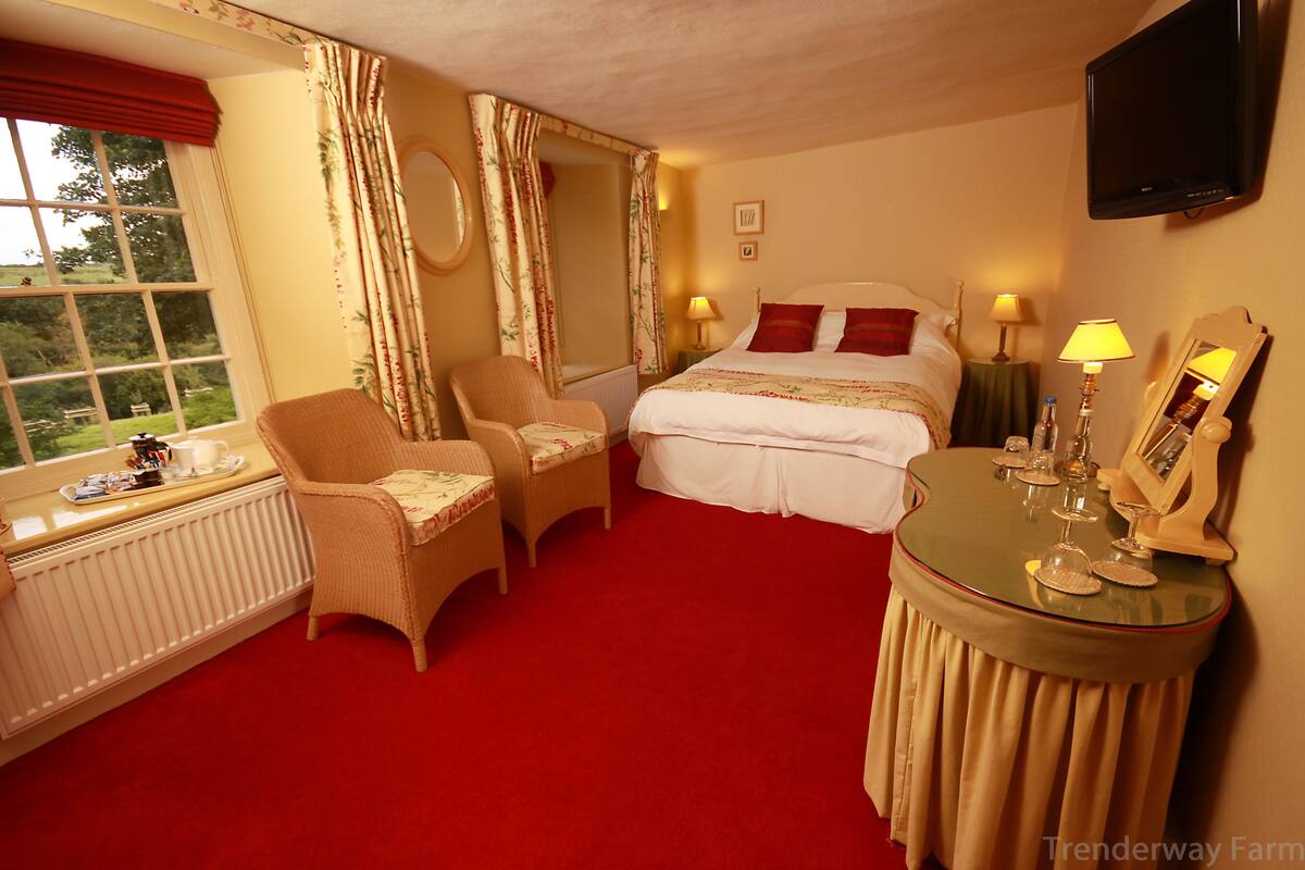 A hotel room with a large bed, two chairs, a small table with a mirror, and a window with curtains.