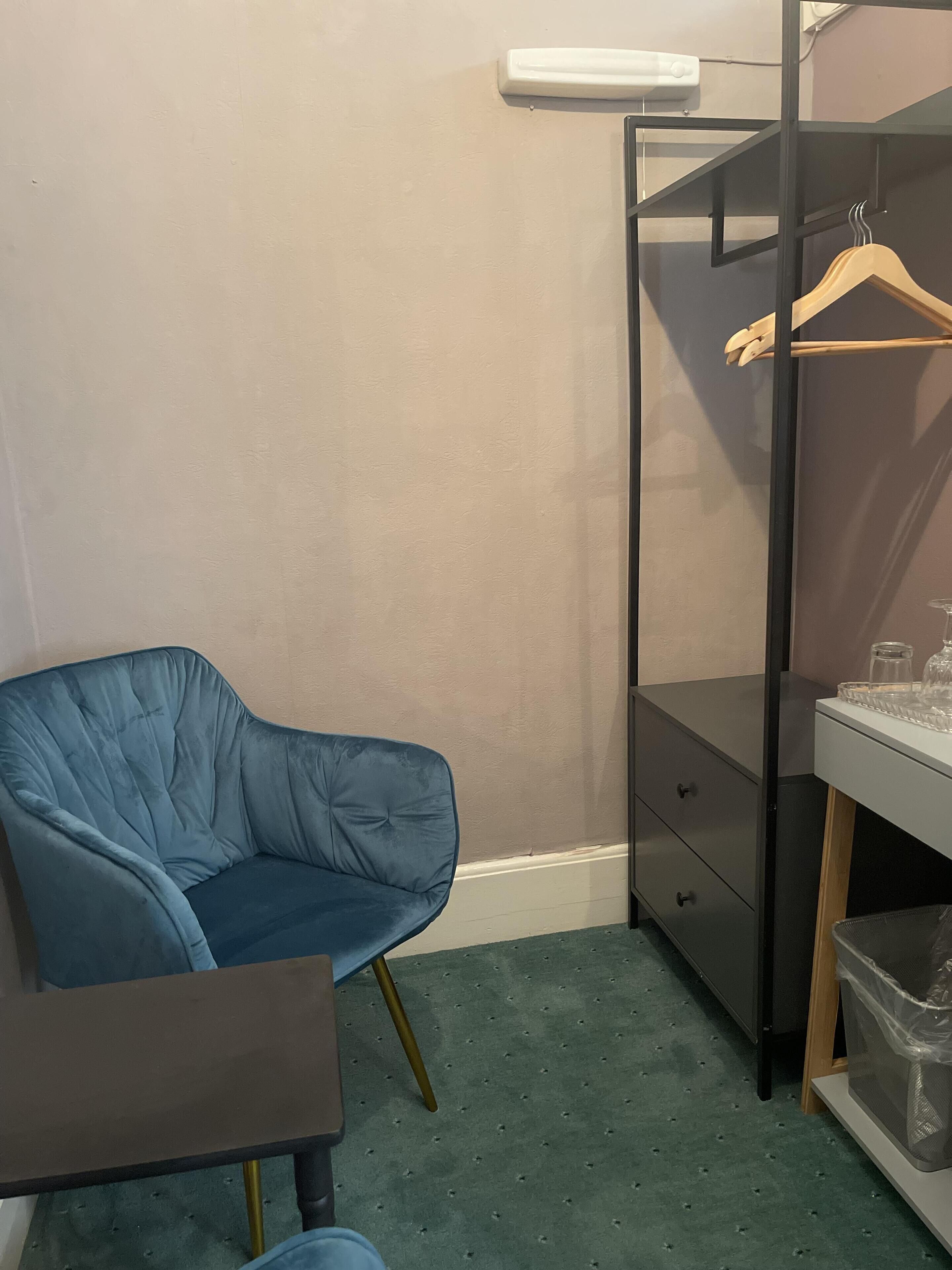 Une pièce comprenant une chaise bleue, une petite table, une armoire noire et une table de chevet blanche avec un ensemble de verres.