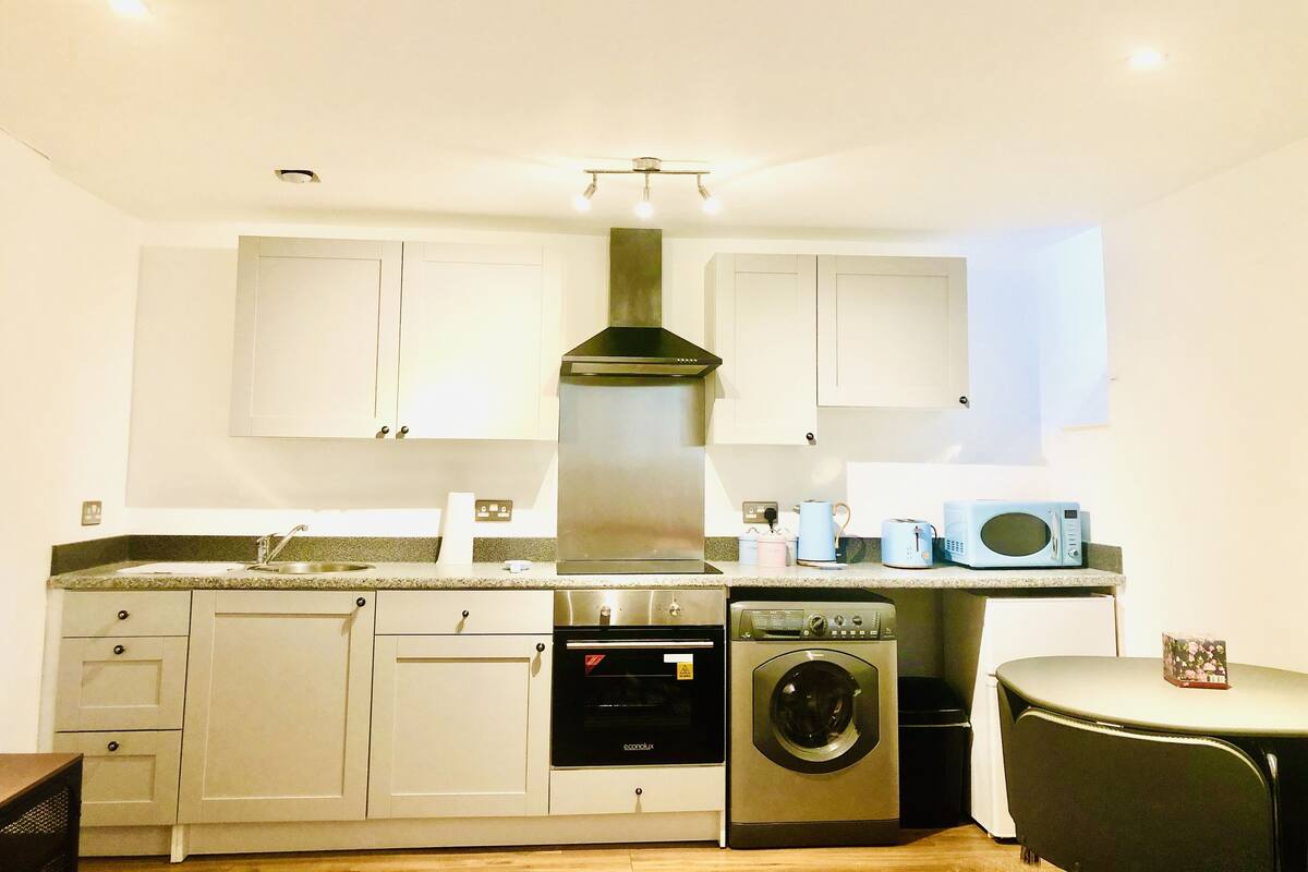 A compact kitchen with white cabinets, a stainless steel range hood, an oven, a washing machine, and a microwave.