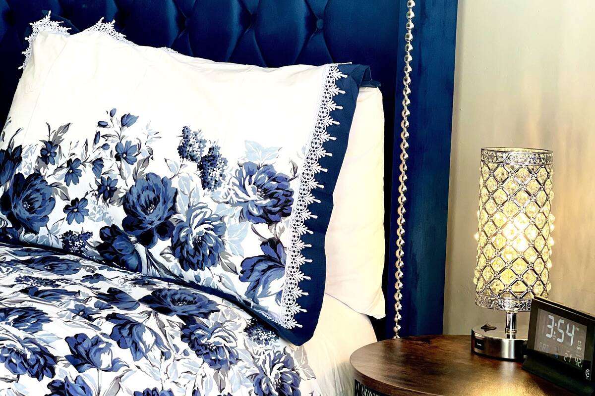 A bedroom with a tufted headboard, floral bedding, a bedside lamp, and a clock.