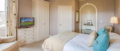 Une chambre à coucher avec un lit, une télévision, une armoire, une porte et une lampe.