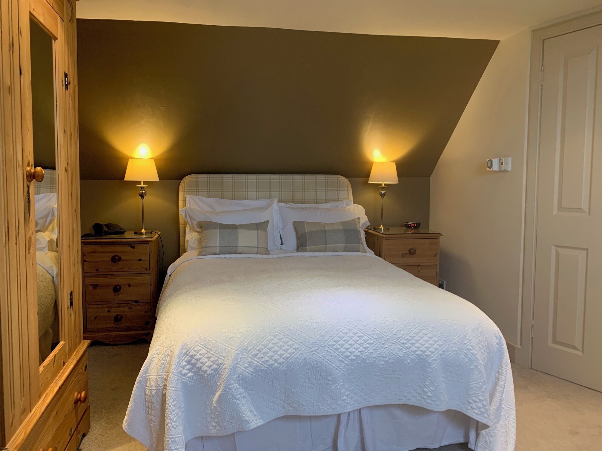 A bedroom with a bed, two bedside tables, a nightstand, a wooden wardrobe, and a door.