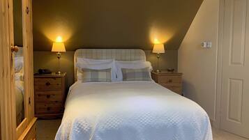 A bedroom with a bed, two bedside tables, a nightstand, a wooden wardrobe, and a door.