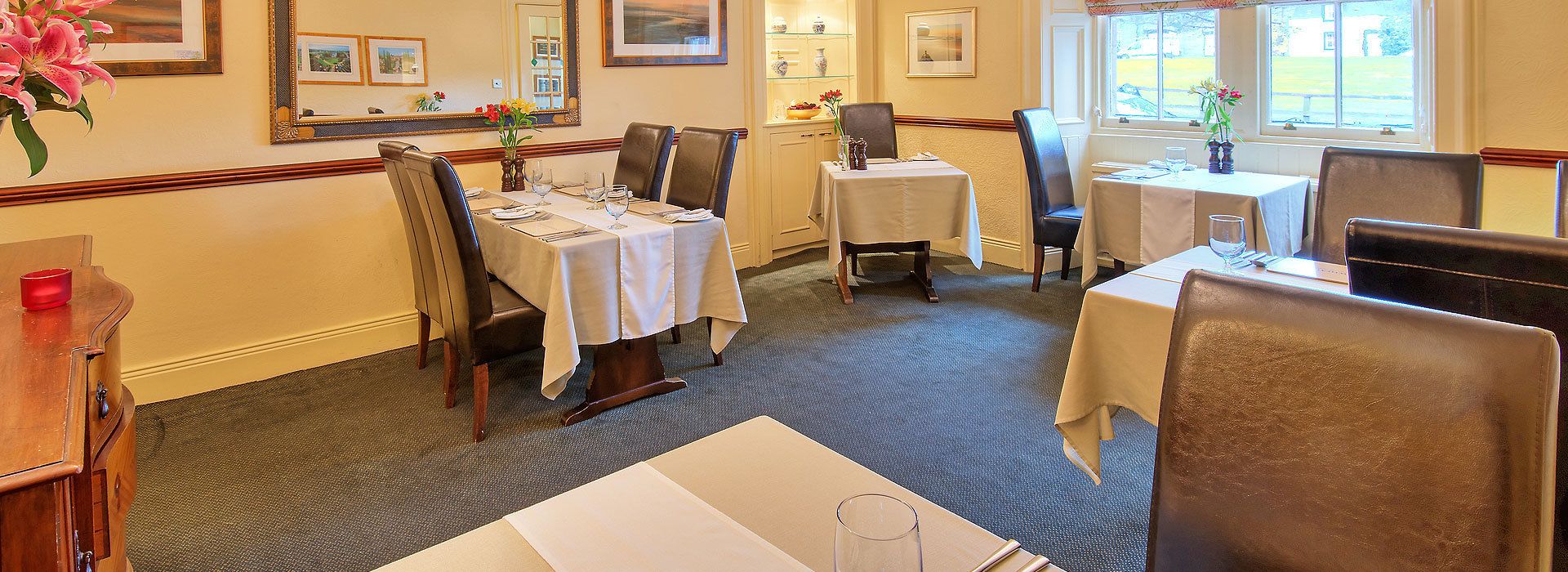 A dining area with tables set for four, chairs, and a vase of flowers.