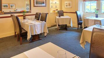 A dining area with tables set for four, chairs, and a vase of flowers.
