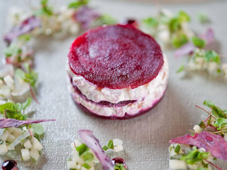 A beetroot-based dish with a creamy layer, surrounded by fresh greens and herbs.