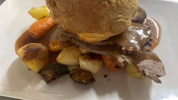 Um prato com sanduíche de carne assada, legumes assados e molho gravy.