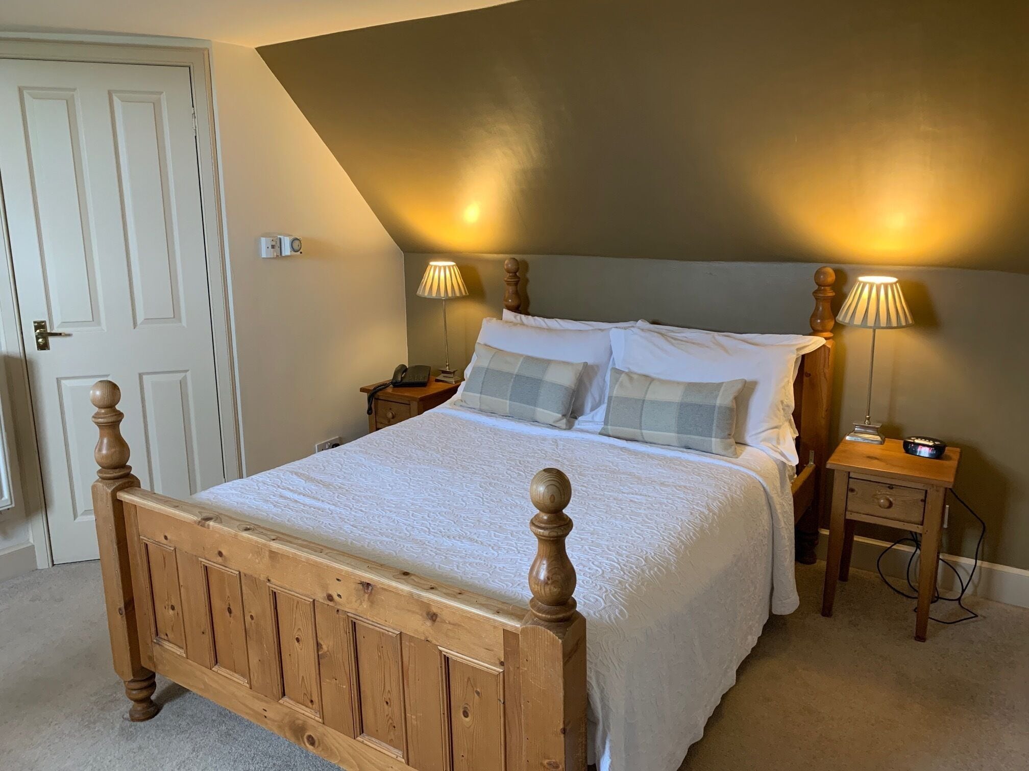 A bedroom with a wooden bed, two bedside tables, a nightstand, a door, and a sloped ceiling.