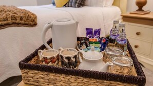 Een rieten mand met mokken, een theepot en flessen op een nachtkastje in een hotelkamer.