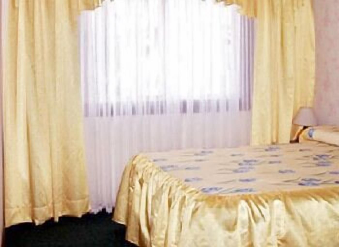 A hotel room with a bed, curtains, and a lamp.